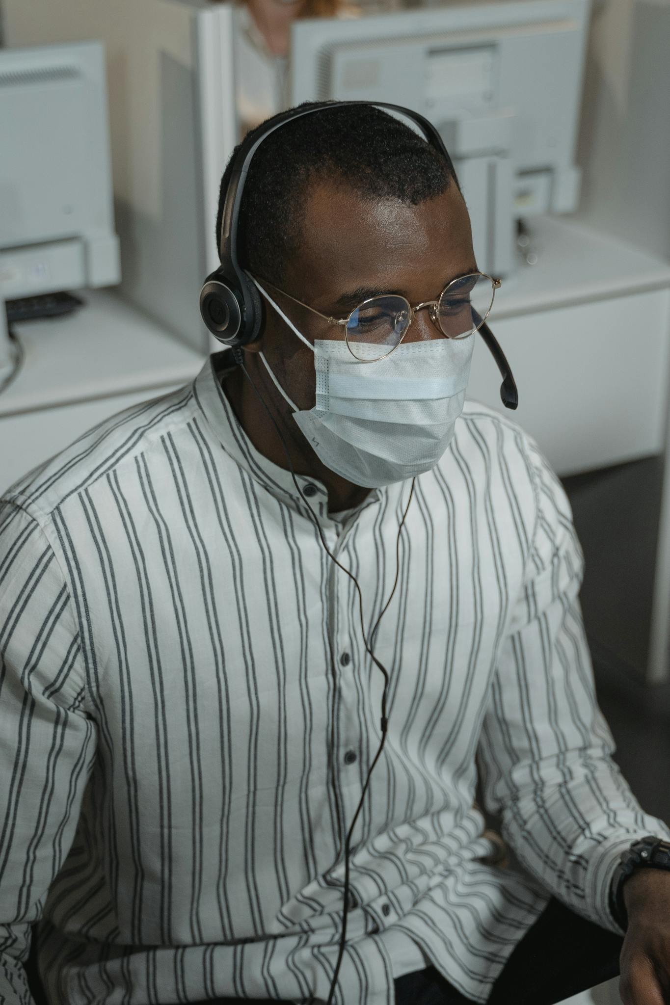 African American male working in a call center with headset and face mask.