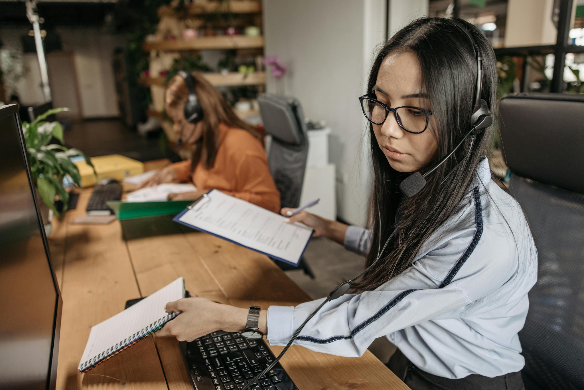 Focused call center agent wearing headset, managing paperwork at office desk.